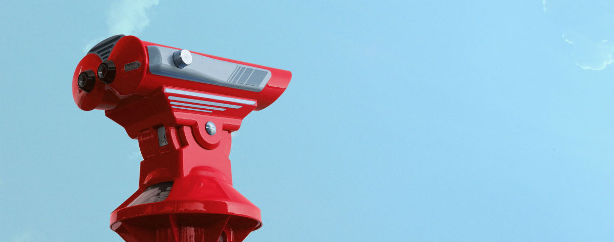 Red binoculars at a tourist attraction against a blue sky